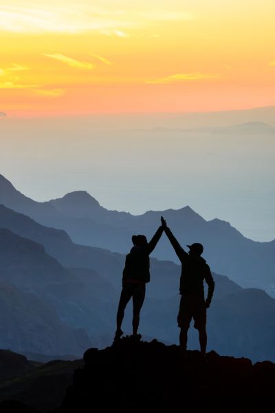 2 people on top of a mountain with a sunset doing a high-five